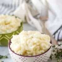 Decorative bowls loaded with Instant Pot risotto surrounded by herbs.