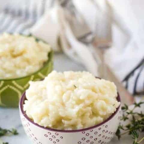 Decorative bowls loaded with Instant Pot risotto surrounded by herbs.