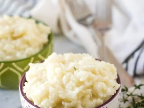 Decorative bowls loaded with instant pot risotto surrounded by herbs.