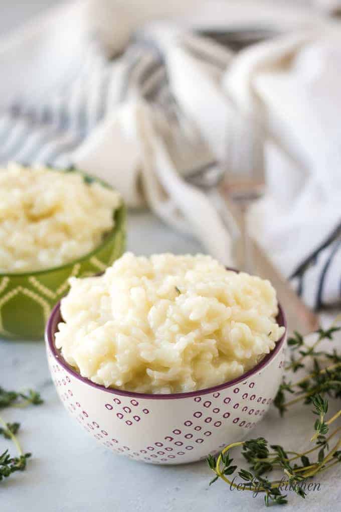 Decorative bowls loaded with Instant Pot risotto surrounded by herbs.