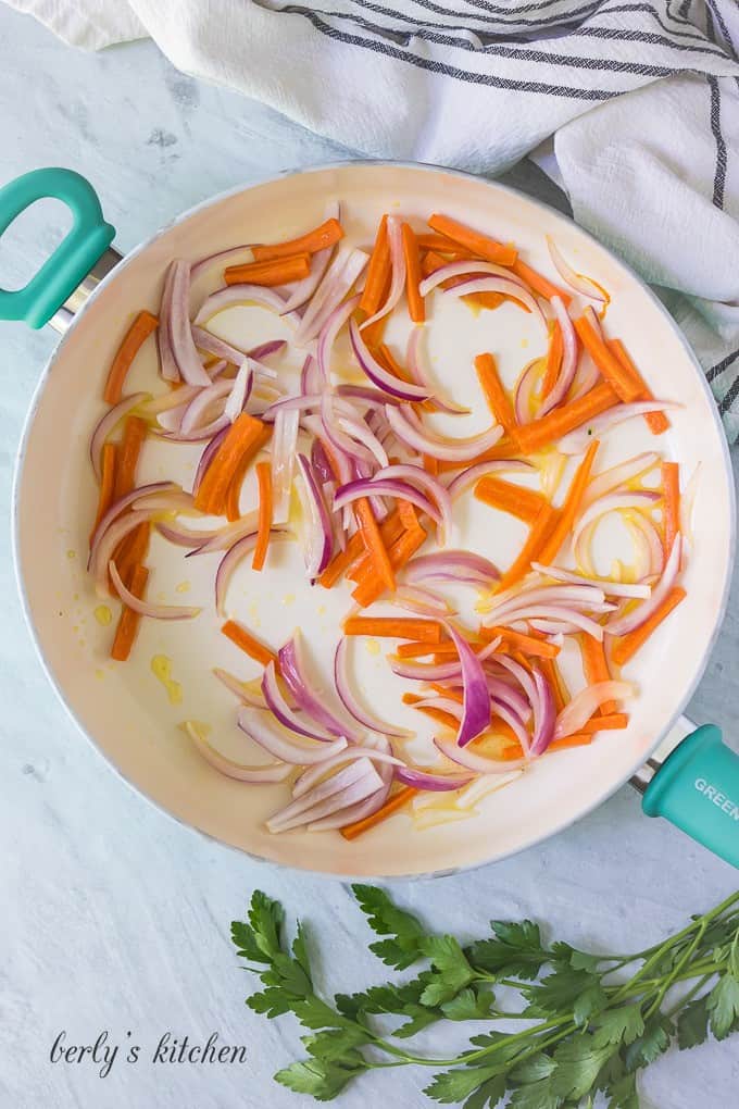 Thinly sliced carrots and red onions sauteed in a large skillet.
