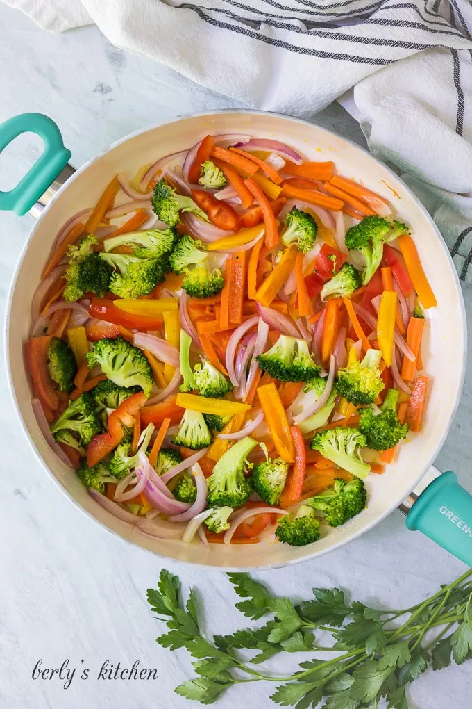 Broccoli florets and sliced bell peppers have been added to the skillet.