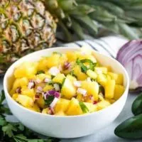 The pineapple salsa, served in a bowl, surrounded by fresh ingredients.