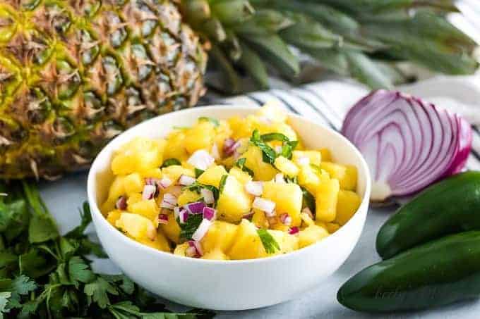 The pineapple salsa, served in a bowl, surrounded by fresh ingredients.