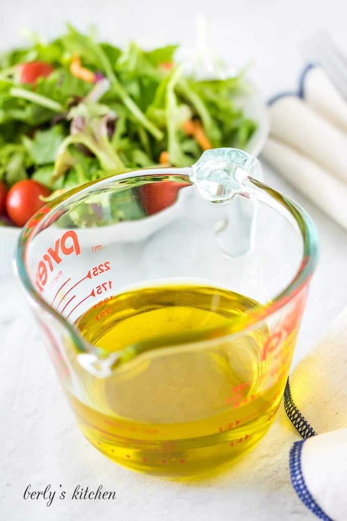 A glass measuring cup with ¾ of a cup of olive oil.