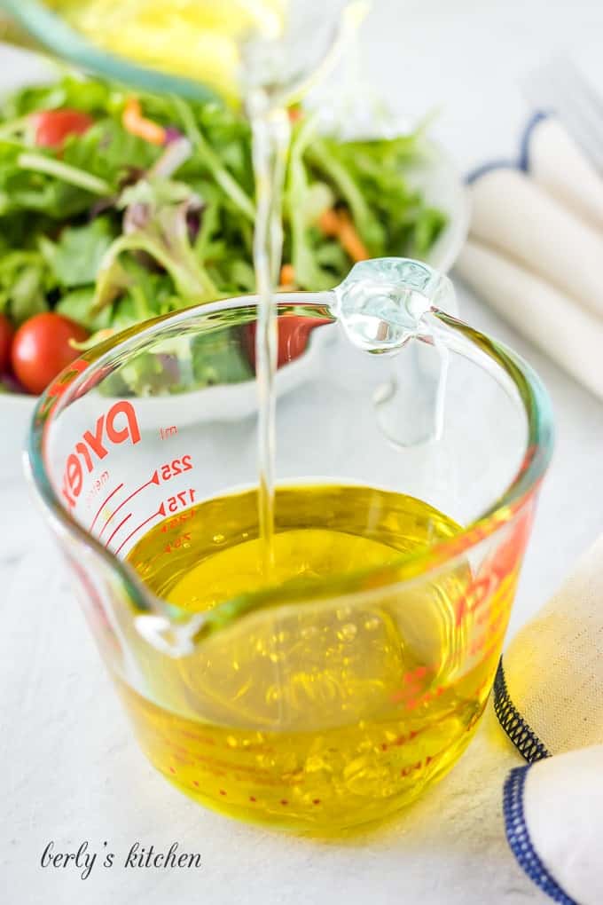 The white wine vinegar being added to the olive oil.