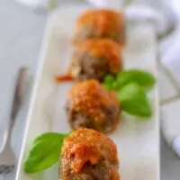 The meatballs, topped with red sauce, on a rectangular plate.