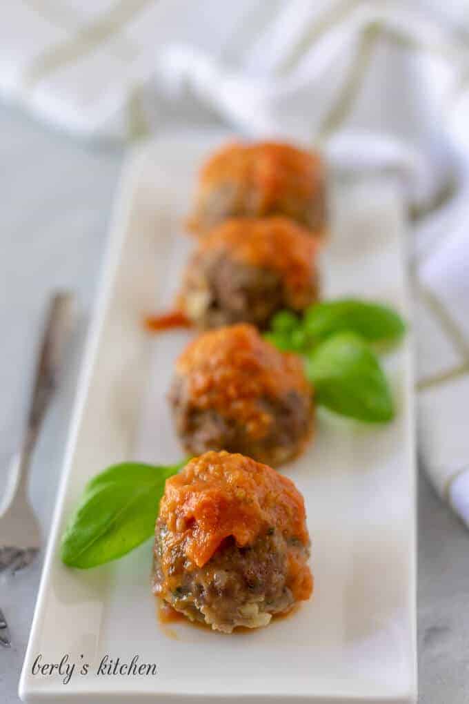 The meatballs, topped with red sauce, on a rectangular plate.