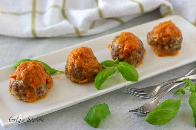 Four oven baked meatballs on a rectangular plate topped with red sauce.