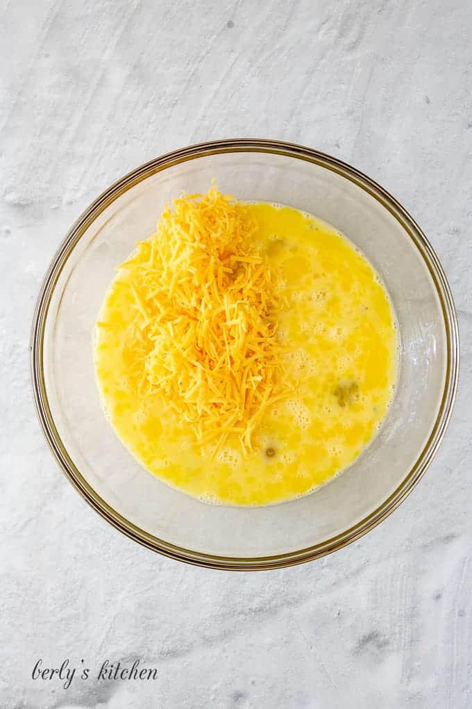 Whisked eggs and cheese in a large glass mixing bowl.
