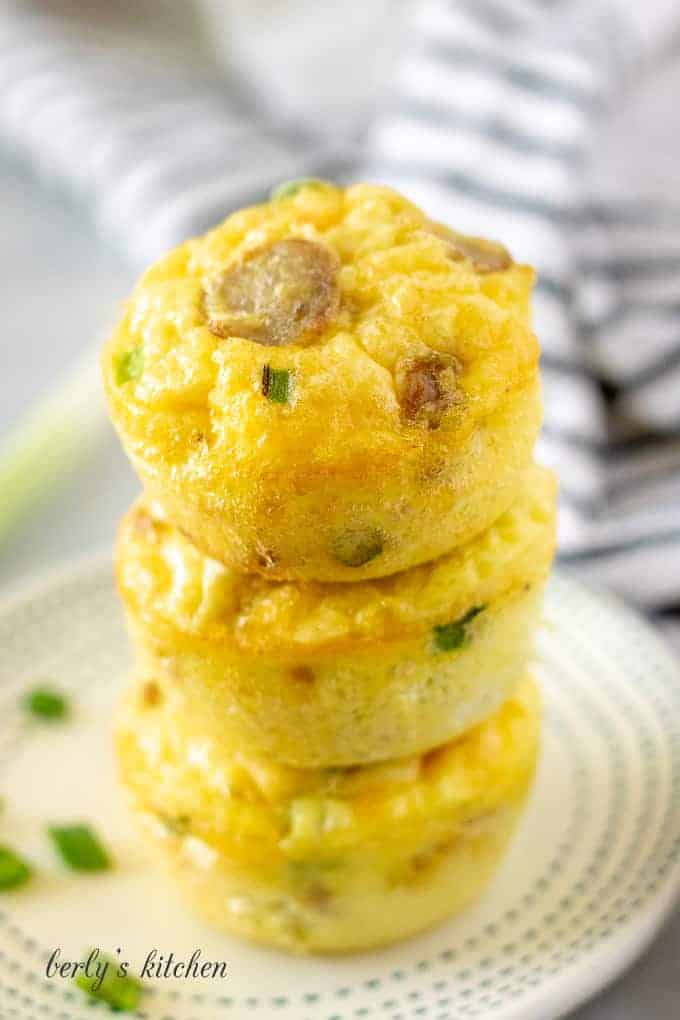 Three sausage egg and cheese muffin cups stacked on a plate.