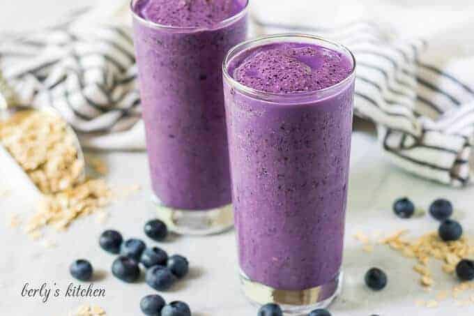 Two blueberry smoothies in large glasses accented with fresh berries.
