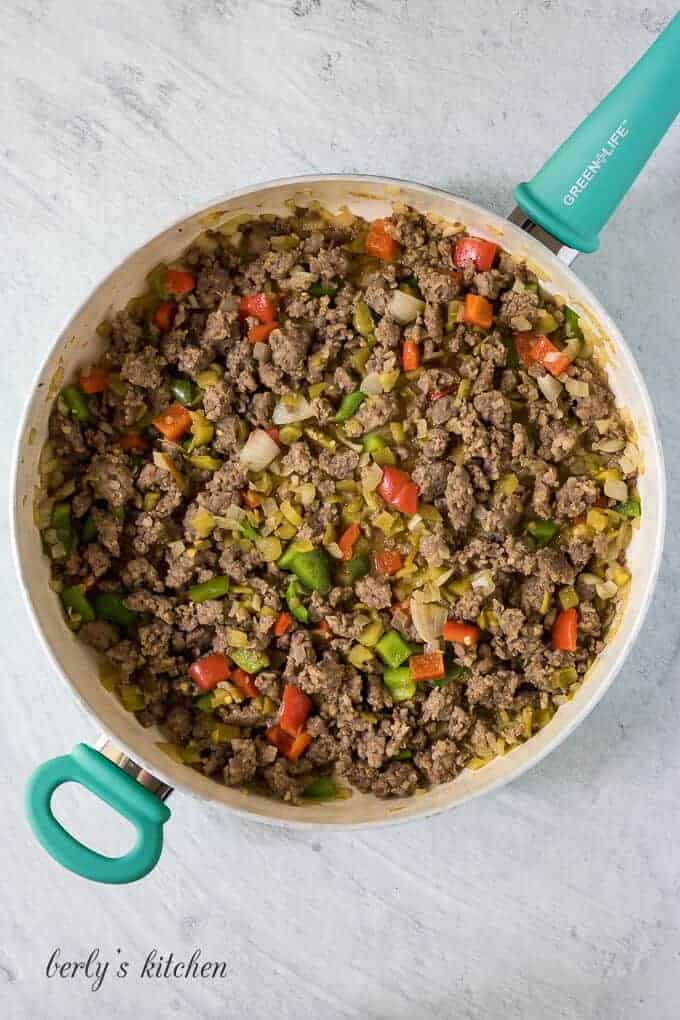 The ground pork, onions, and peppers cooking in a skillet.