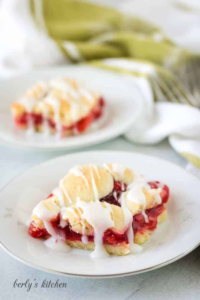 Two cherry bars, topped with almond icing, served on plates.