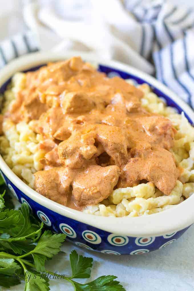 A blue bowl filled with chicken paprikash and cooked spaetzle.