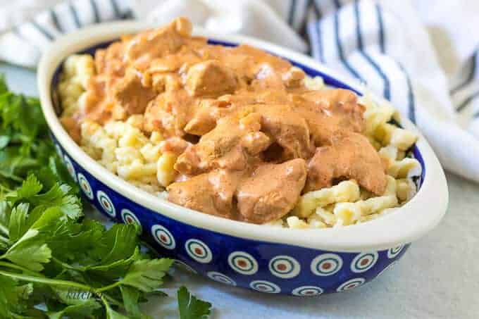 Paprika chicken served on spaetzle in a decorative blue bowl.