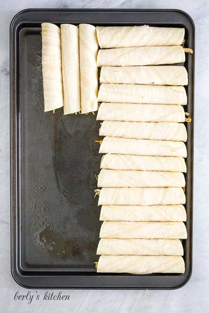Filled tortillas have been rolled and placed on a baking sheet.