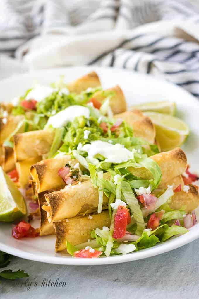 The baked chicken taquitos topped with lettuce, tomatoes, and guacamole.