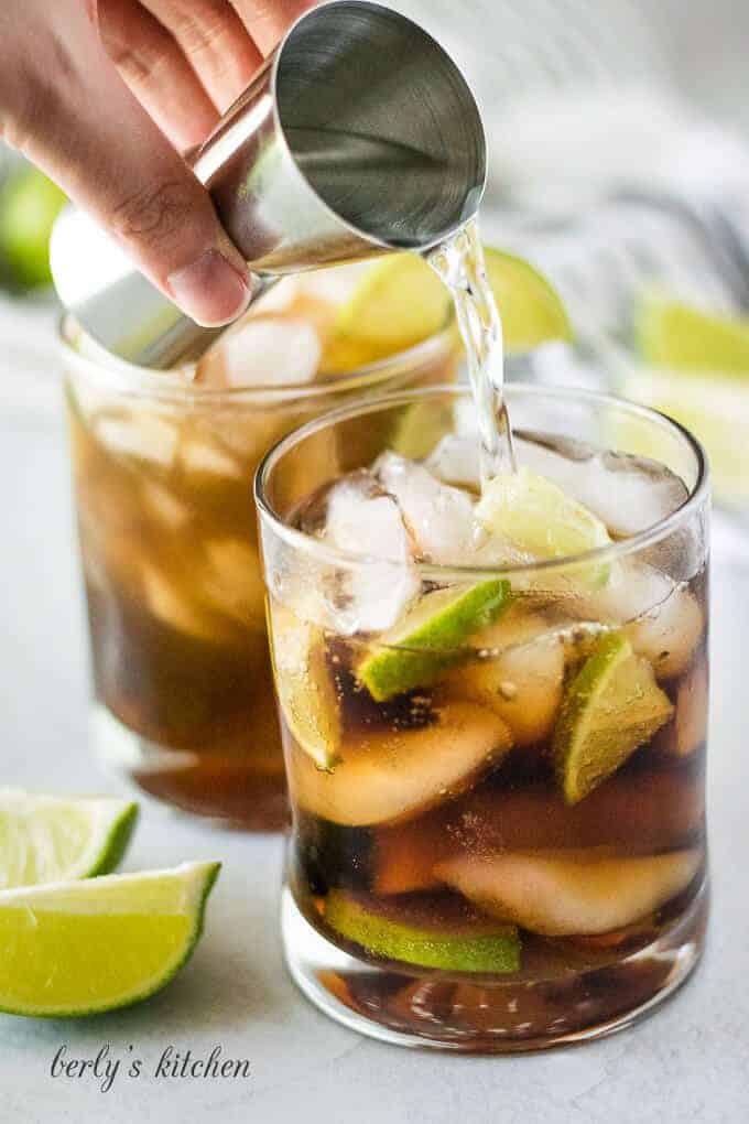 The rum being added to the cola in a low ball glass.