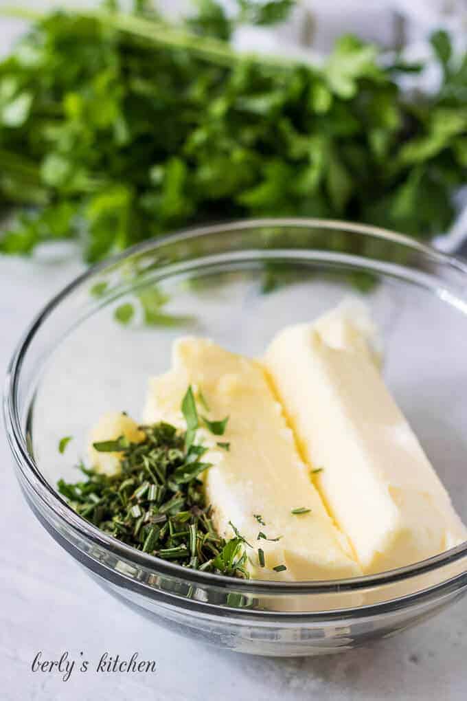 Softened unsalted butter and chopped herbs in a mixing bowl.