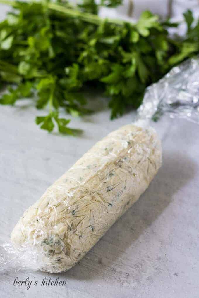 The compound butter has been rolled into a log in plastic wrap.