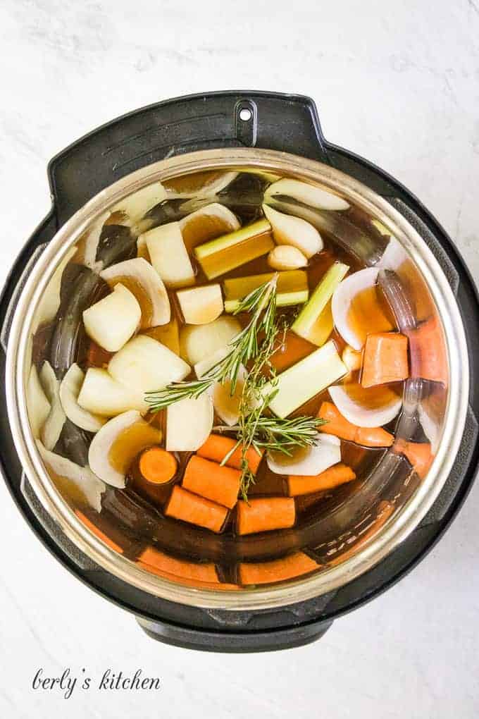 The broth, herbs, and vegetables in the pressure cooker liner.