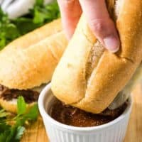 The French dip sandwich being dipped in a side of au jus.