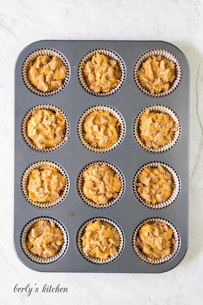 Twelve muffin liners have been half filled with raw batter.