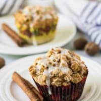 Two muffins, on plates, garnished with a fresh cinnamon stick.