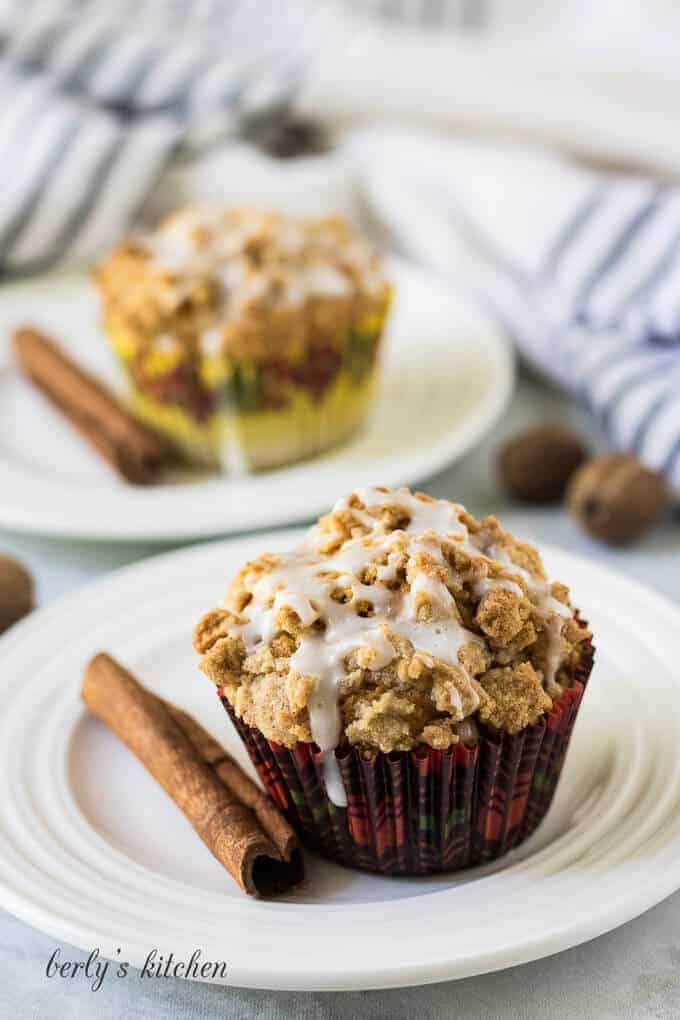 Two muffins, on plates, garnished with a fresh cinnamon stick.