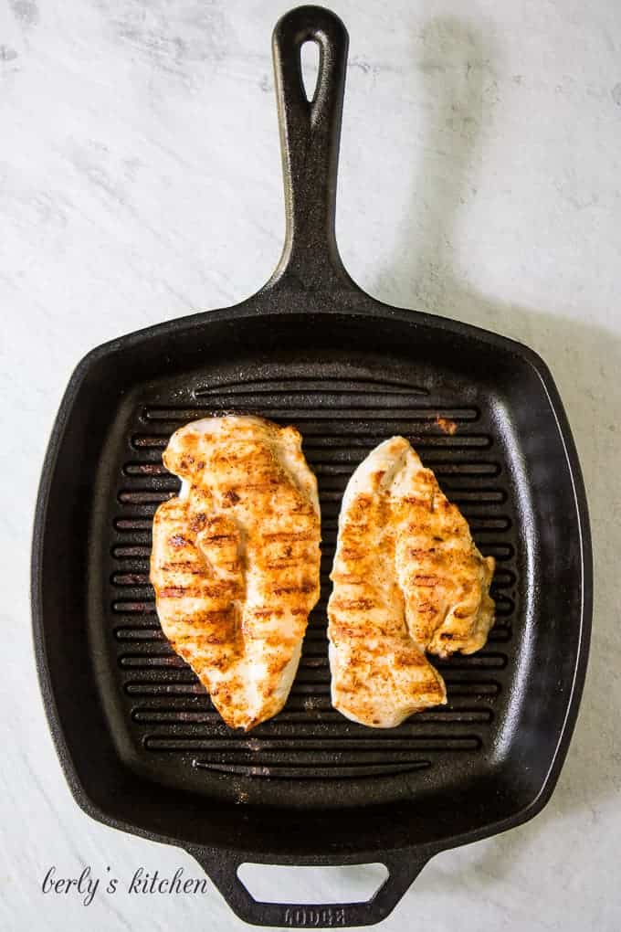 Two large pieces of chicken breast grilling on a griddle.