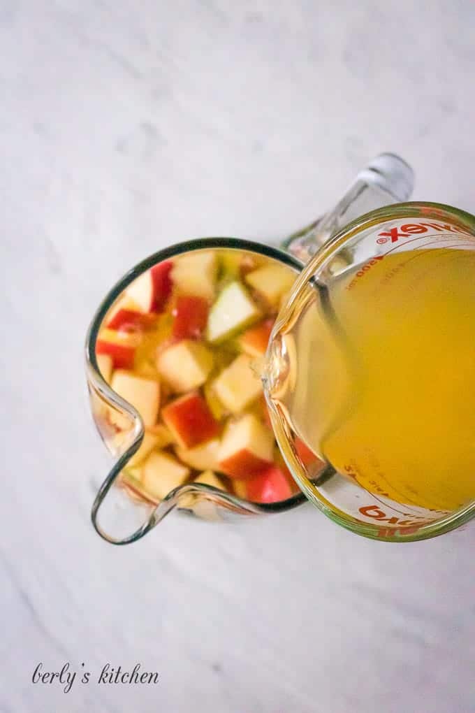 The apple cider being poured into the pitcher with wine.