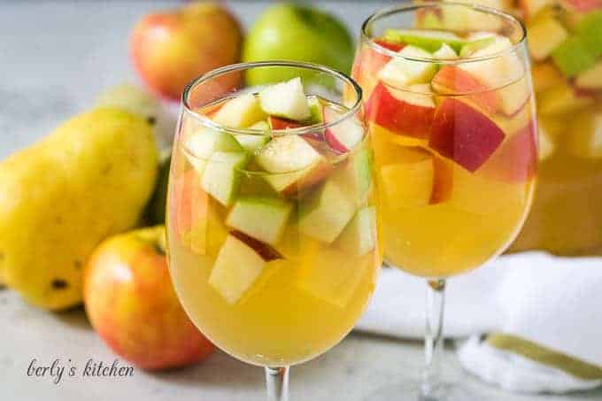 Two glass of apple sangria served in white wine glasses.