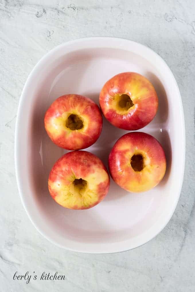 Four washed and cored apples in a large baking dish.