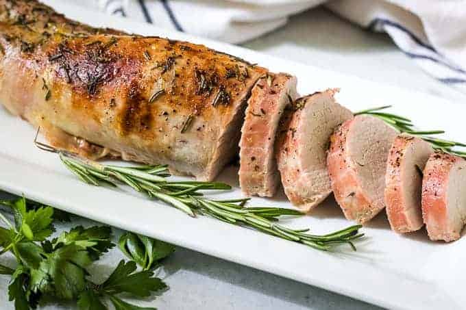 The pork tenderloin has been sliced and garnished with rosemary.