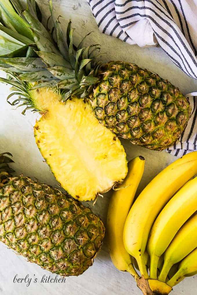 Fresh bananas and pineapples decoratively arranged on a marble table.