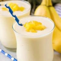 Two finished banana pineapple smoothies garnished with diced fresh pineapple.