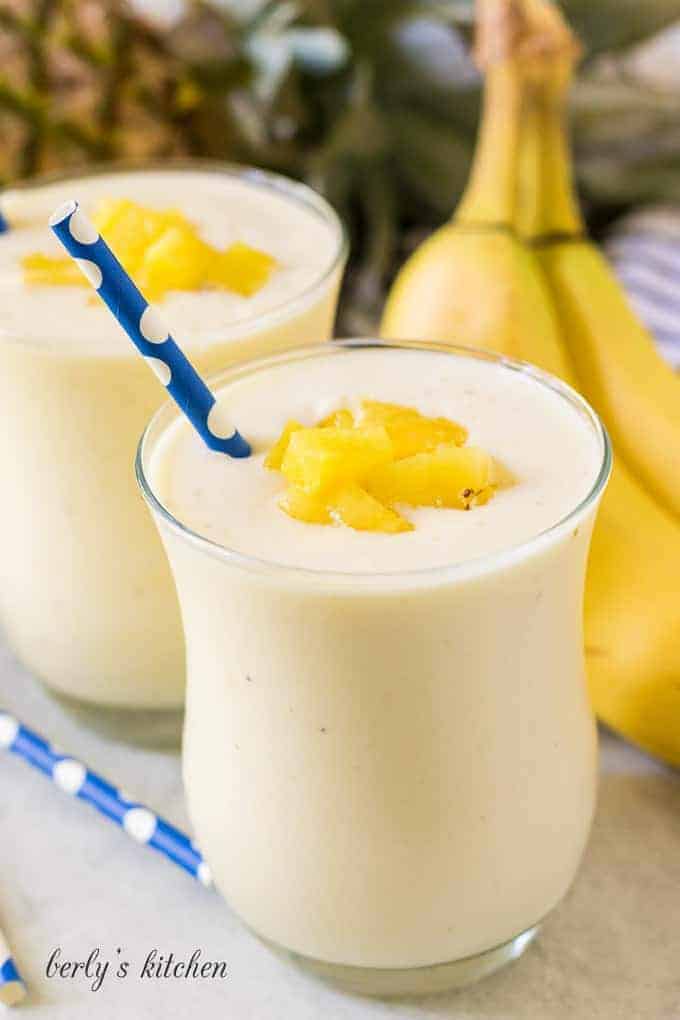 Two finished banana pineapple smoothies garnished with diced fresh pineapple.