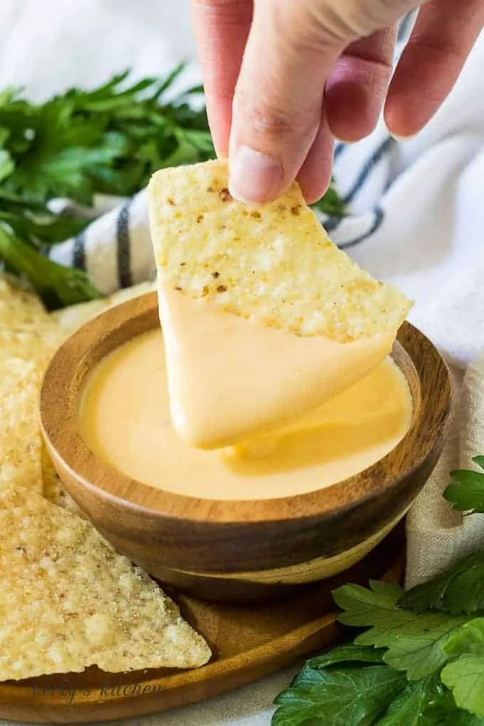 A tortilla chip being dipped into the finished cheese dip.