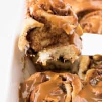 A baked cinnamon roll being scooped from the baking dish.