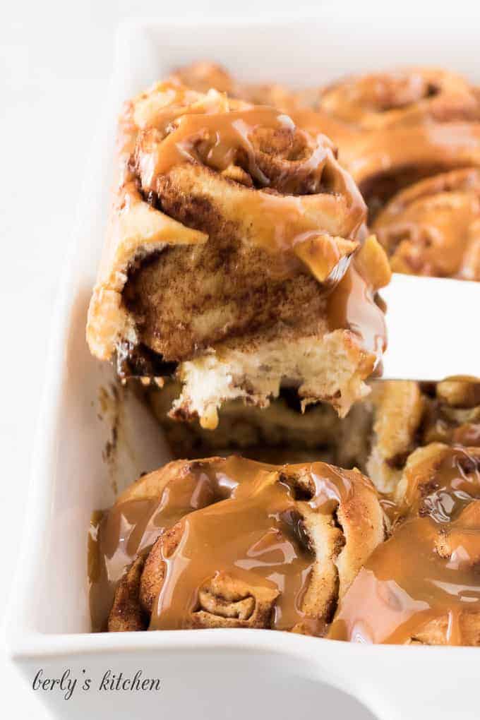 A baked cinnamon roll being scooped from the baking dish.