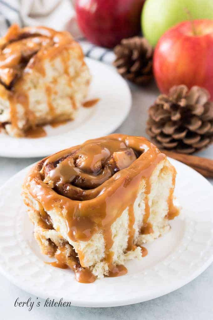 Two cinnamon rolls, on plates, topped with warm caramel sauce.