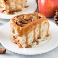 One finished apple cinnamon roll drizzled with warm caramel sauce.