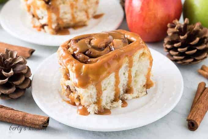 One finished apple cinnamon roll drizzled with warm caramel sauce.