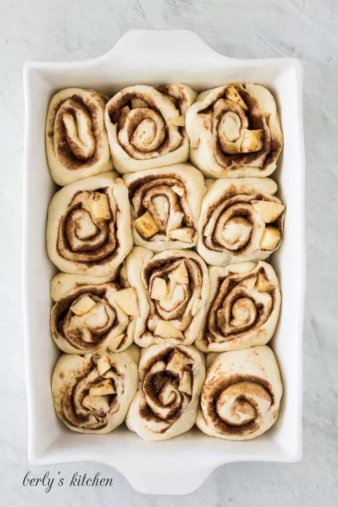 Twelve uncooked apple cinnamon rolls in a large baking dish.
