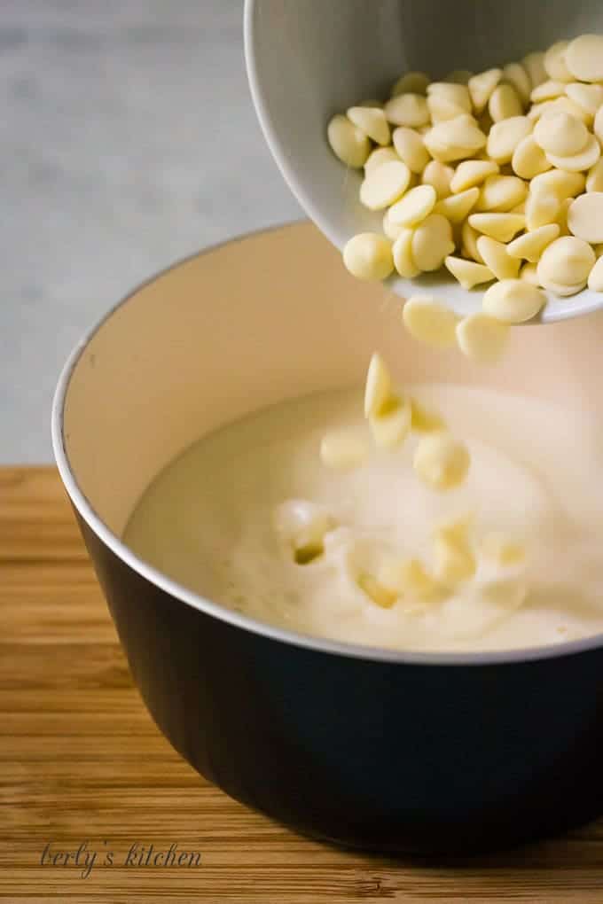 The white chocolate chips being poured into the warm milk.