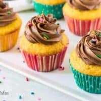 Five cupcakes topped with chocolate buttercream frosting and colorful sprinkles.