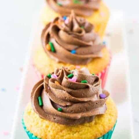 Cake Mix Cupcakes With Chocolate Buttercream Three yellow cupcakes topped with chocolate buttercream frosting and sprinkles.