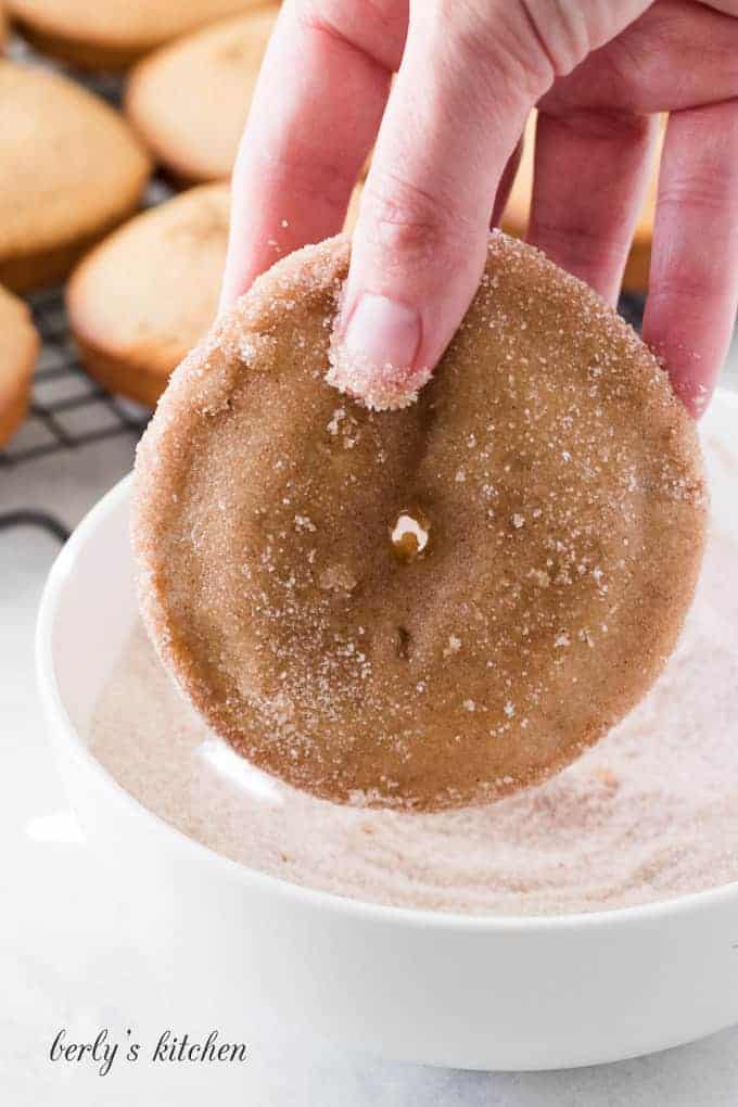 A donut being dipped into the cinnamon and sugar mixture.