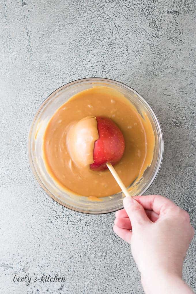 An apple on a skewer being dipped into the caramel.